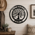 A textured satin black circular metal sign reading "WAYMAKER RANCH" around a central Tree of Life design is centered on a white shiplap entryway wall. A cowboy hat hangs from a coat rack on the left above a rustic wooden bench with a ceramic mug and potted greenery.