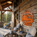 Orange welcome to our cabin metal wall sign with mountain cabin scene displayed on a rustic wood porch wall