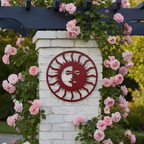 A dark red circular metal sun face sign attached to a white brick pillar, beautifully framed by climbing pink roses growing along a dark blue wooden arbor.