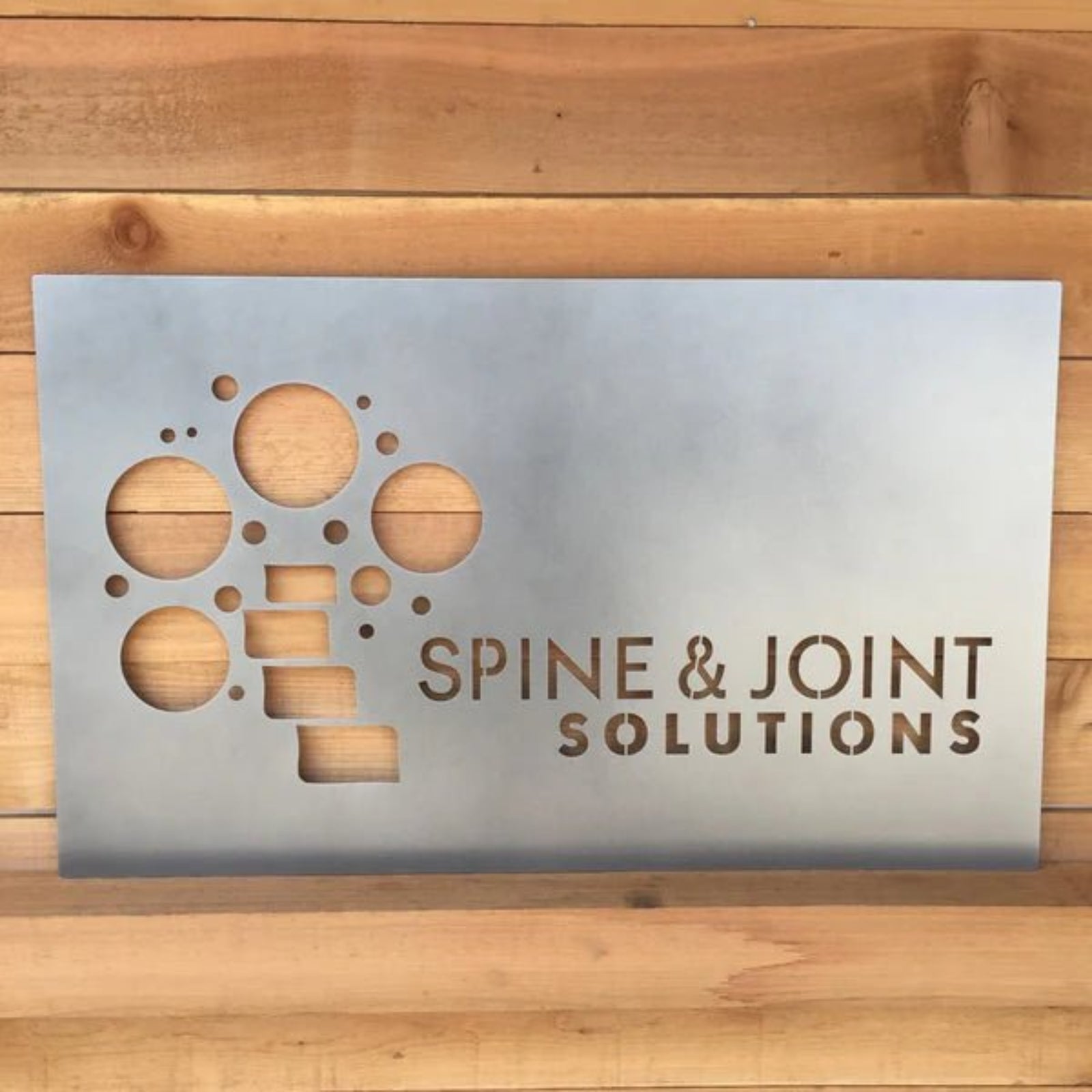 Custom LED office and storefront metal sign featuring “Spine & Joint Solutions” text, precision-cut for professional branding, illuminated business signage, and outdoor display.