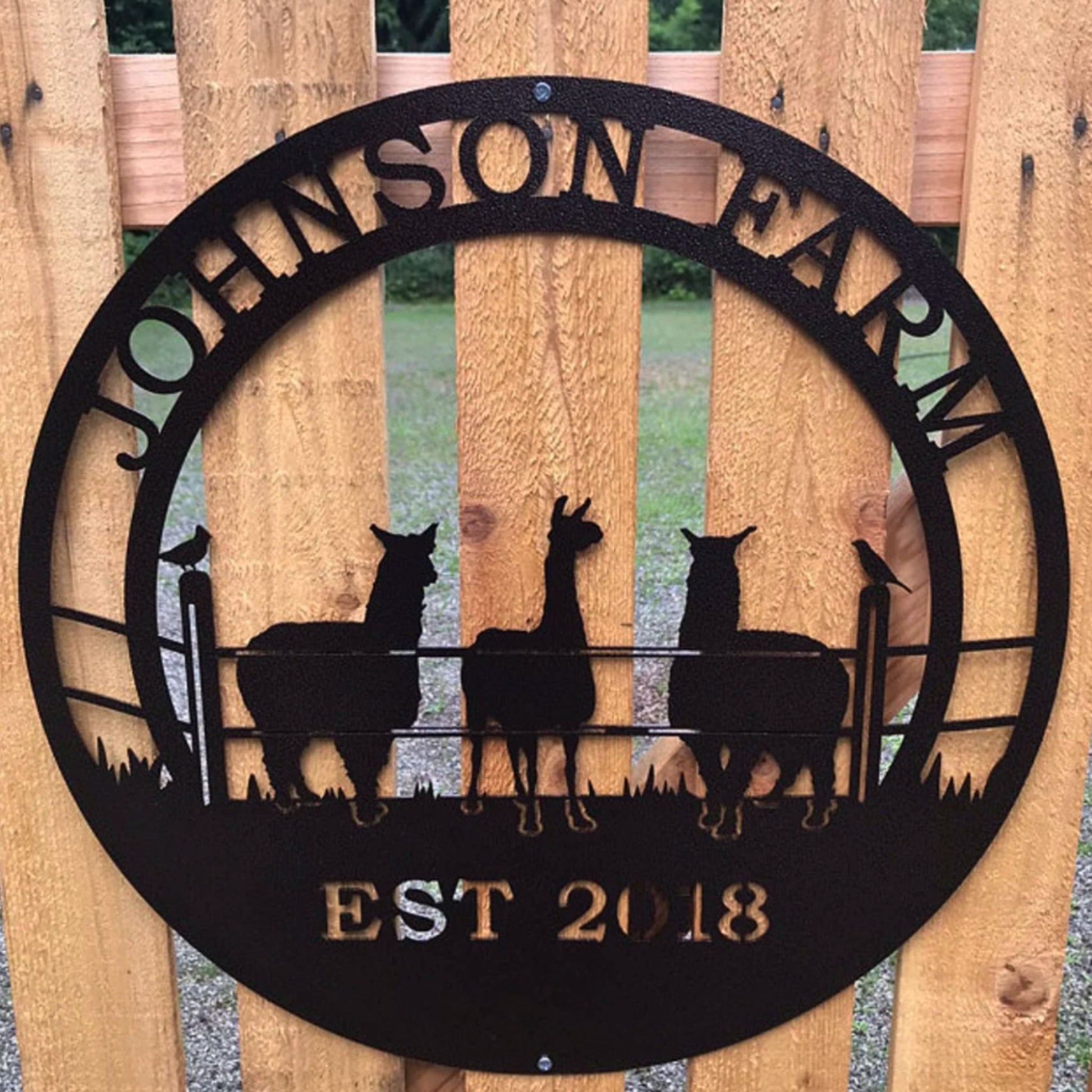 Black custom laser cut metal ranch sign showing three alpacas behind fence, with “JOHNSON FARM EST 2018” text, outdoor farm decor.