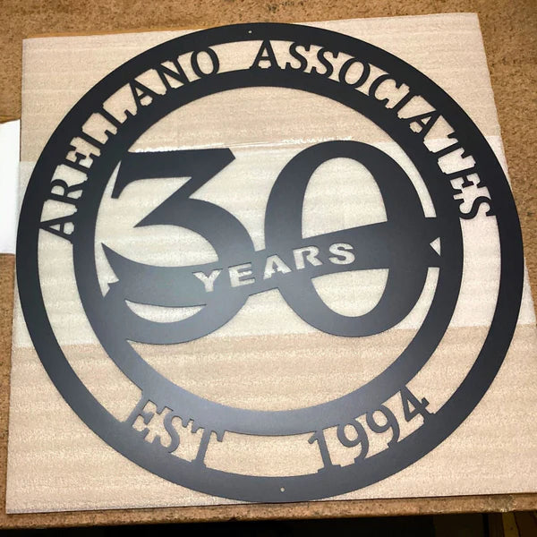Black circular metal sign with “30 YEARS” at center and “ARELLANO ASSOCIATES EST 1994” text encircling the border.