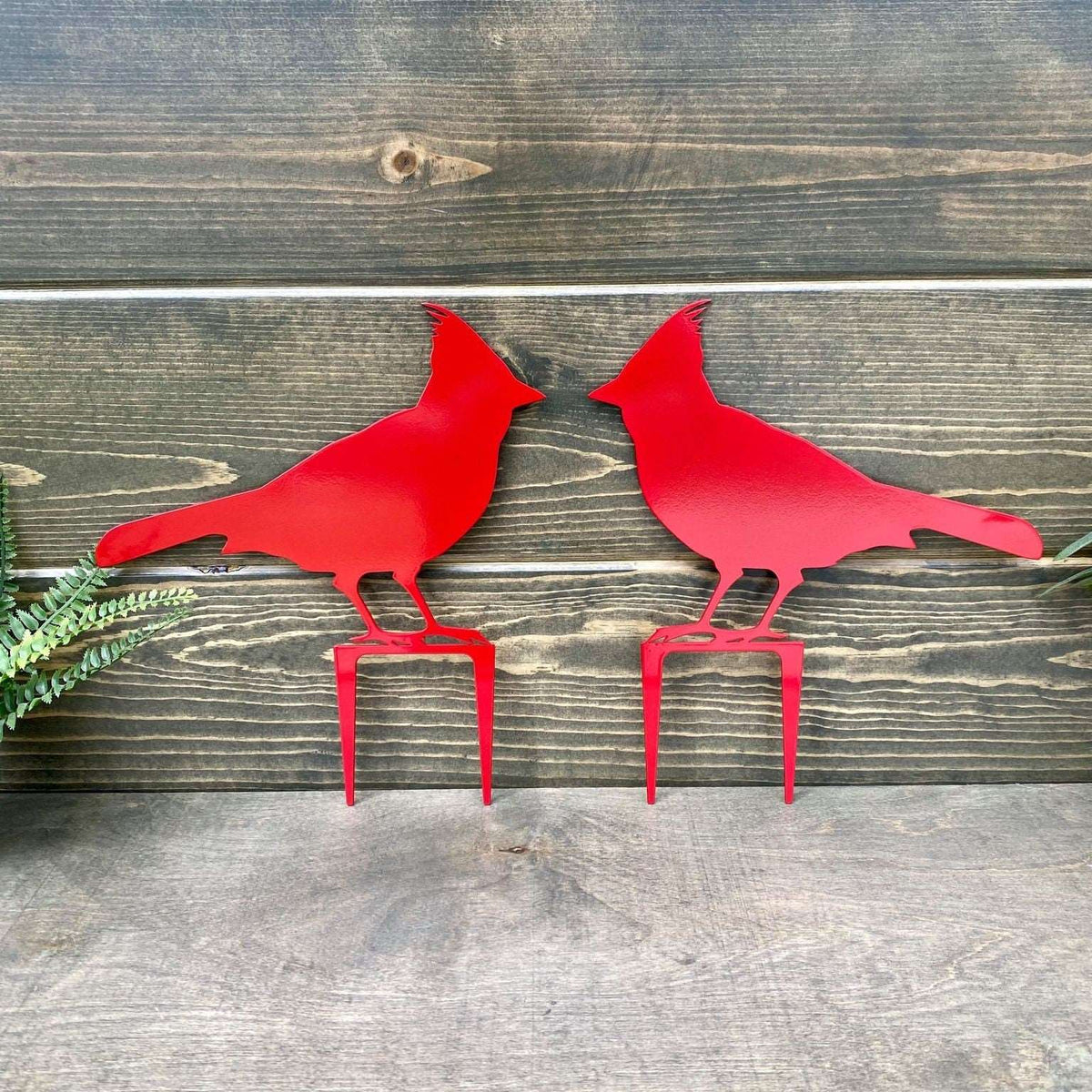 Two matte red metal cardinal bird sculptures on wooden surface, custom outdoor lawn ornament, powder coated steel garden décor, front door farmhouse sign accent