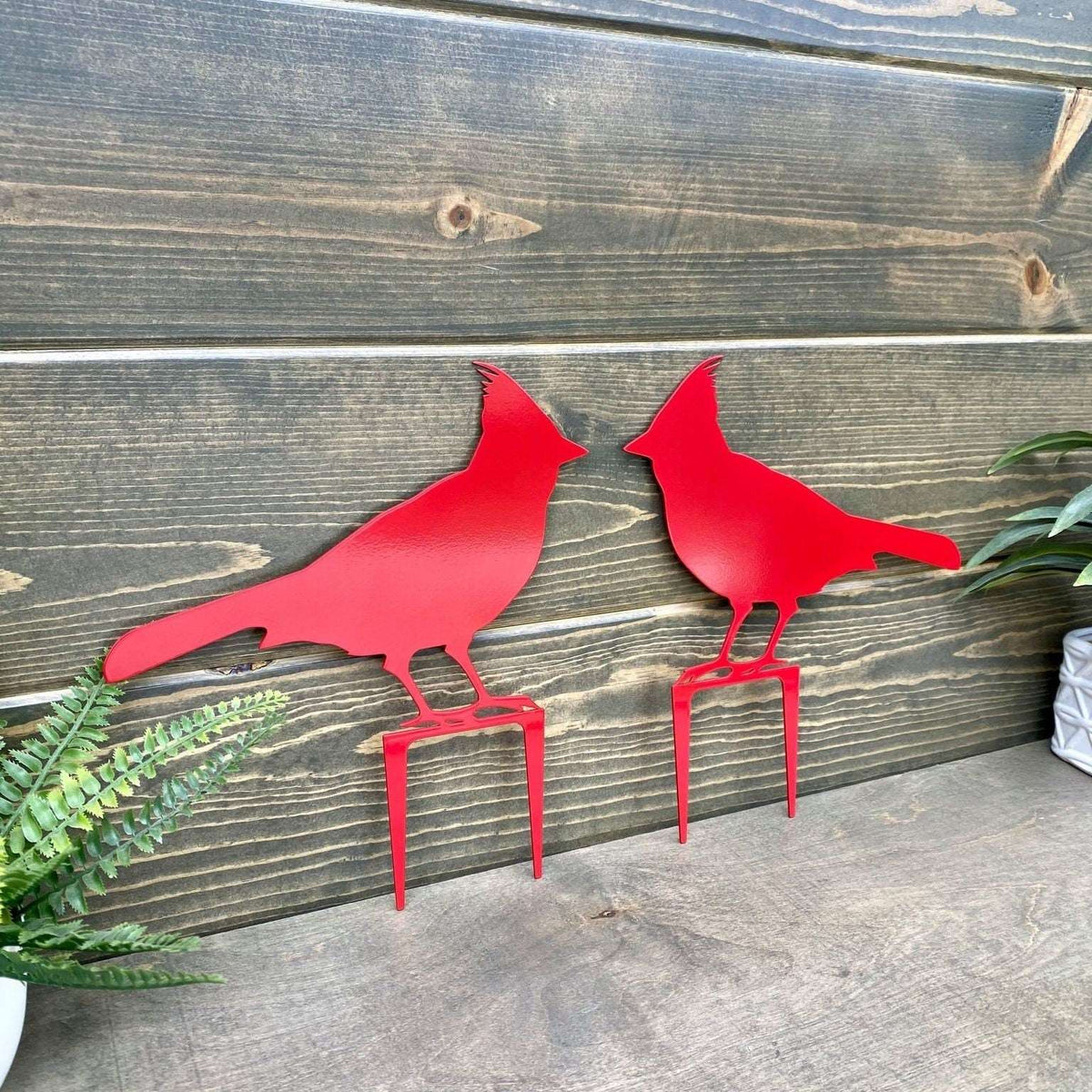 Two matte red metal cardinal bird sculptures against wooden wall, custom outdoor lawn ornament, powder coated steel garden décor, farmhouse front door sign accent