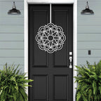 Black front door with white decorative pattern, light blue house exterior, cascading floral wreath door decor, elegant home entry art design