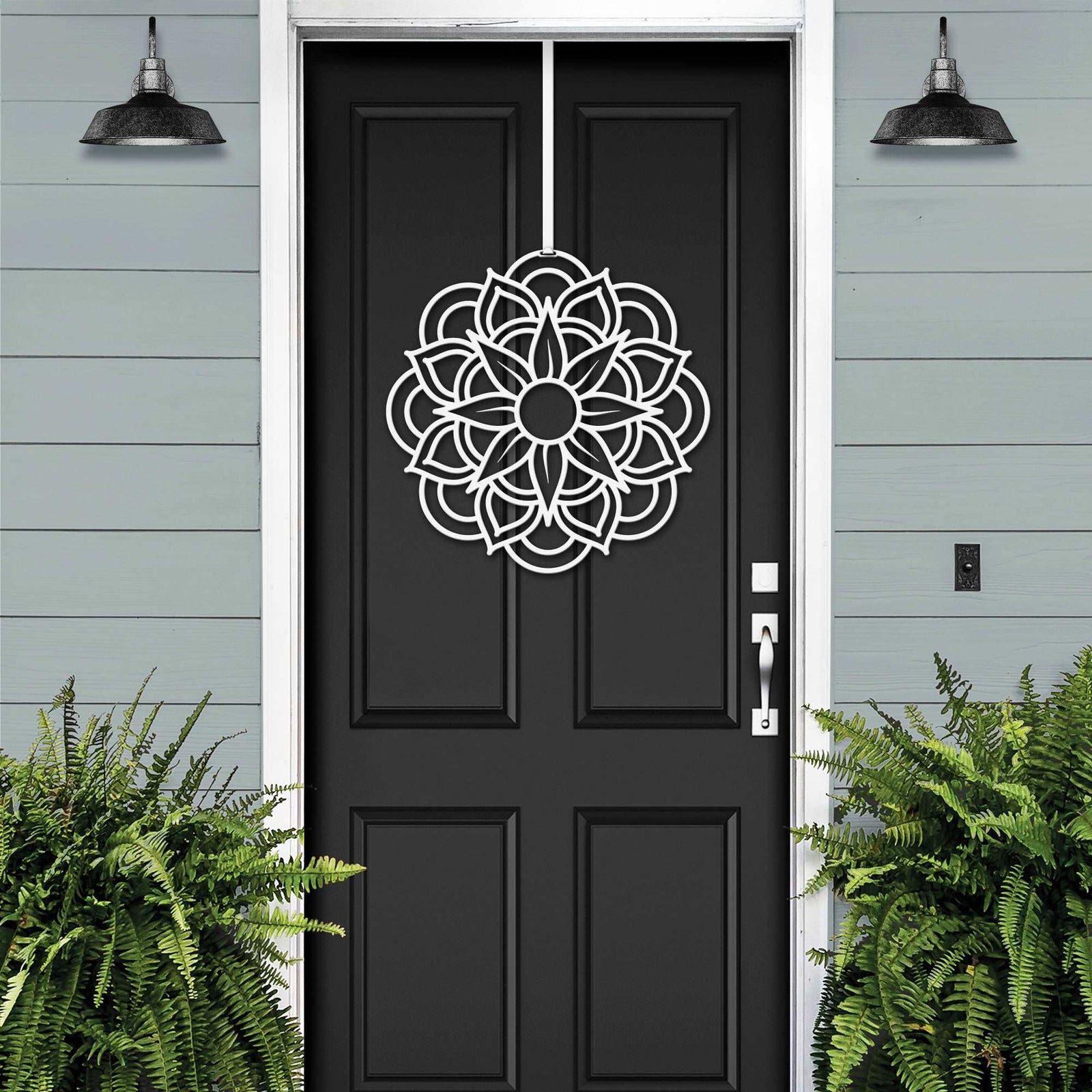 Black front door with white decorative pattern, light blue house exterior, cascading floral wreath door decor, elegant home entry art design