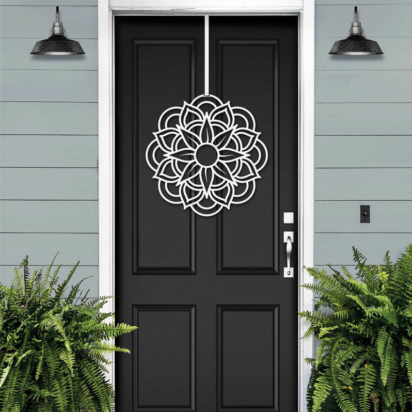 Black front door with white decorative pattern, light blue house exterior, cascading floral wreath door decor, elegant home entry art design