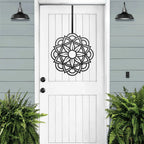 White front door with black decorative pattern, green plants, outdoor lighting, light blue exterior wall, elegant cascading wreath home decor, entryway design art