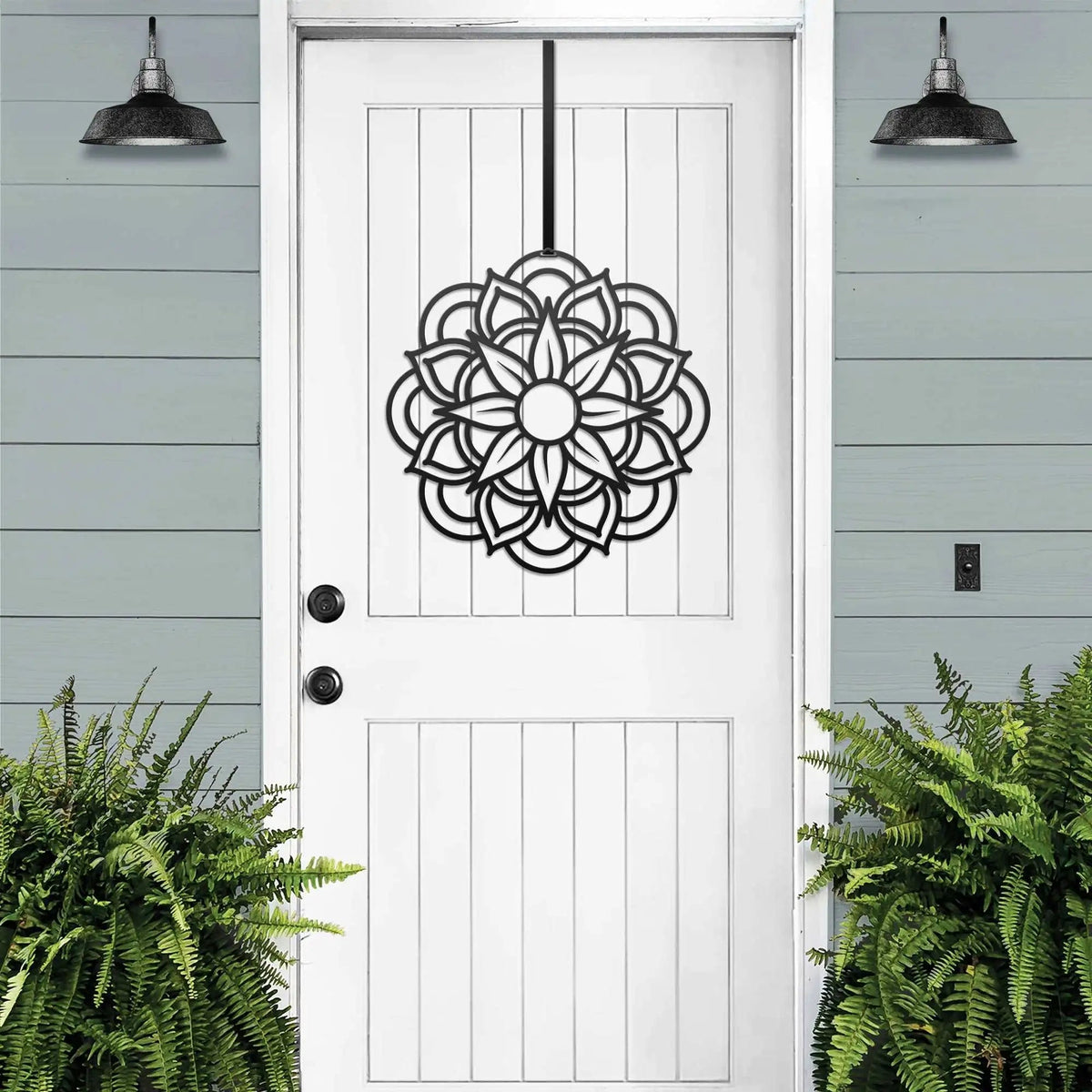 White front door with black decorative pattern, green plants, outdoor lighting, light blue exterior wall, elegant cascading wreath home decor, entryway design art