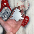 Hand holding a silver Christmas tree ornament against a festive holiday background with green branches, twinkling lights, and seasonal decorations, creating a warm and cheerful Christmas atmosphere.