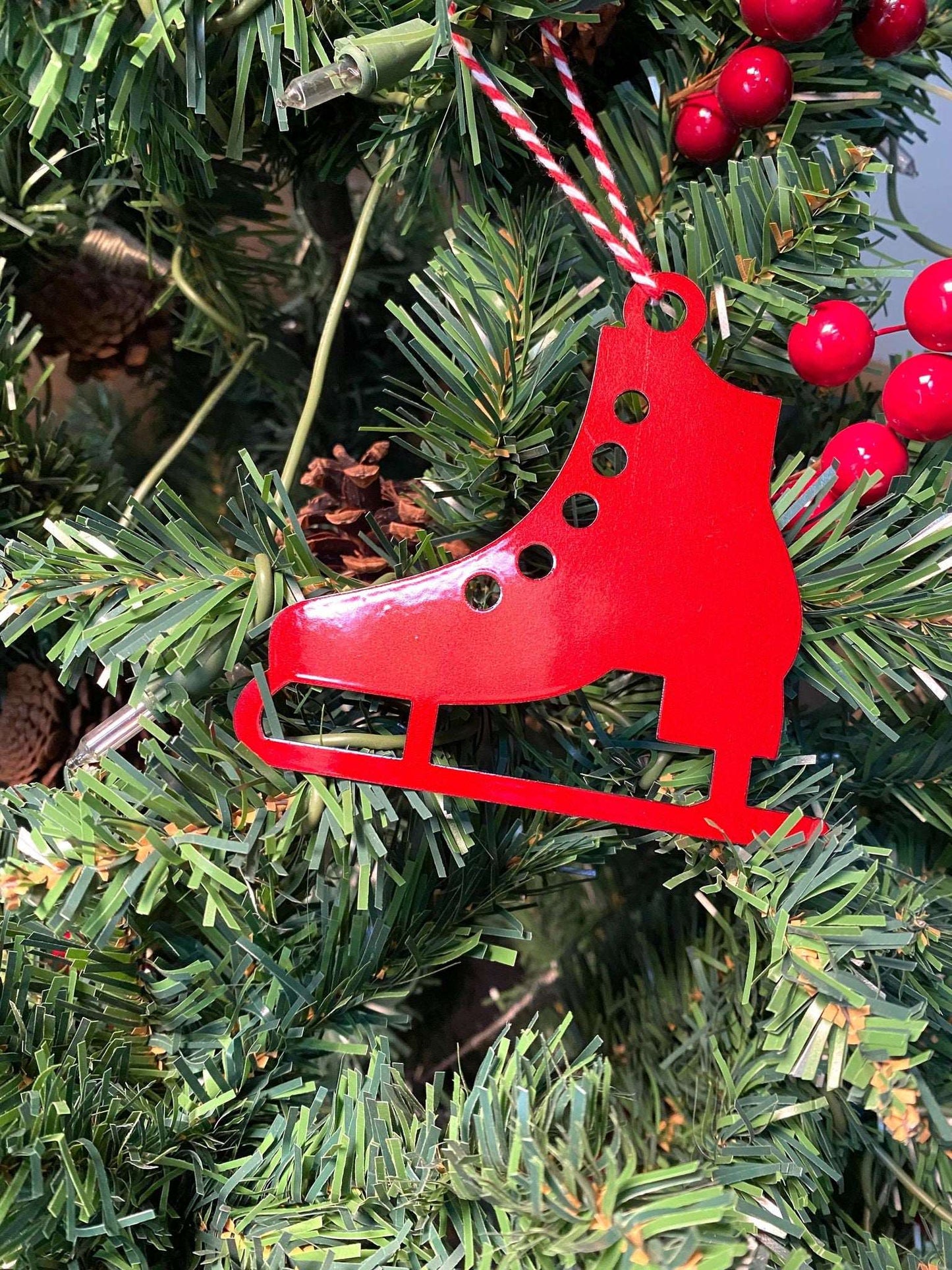 Red ice skate Christmas ornament hanging on a Christmas tree with green leaves and red berries, festive holiday decoration for seasonal home décor