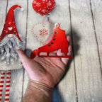 Alt Text: Red metal ice skate Christmas ornament displayed in hand with holiday themed background