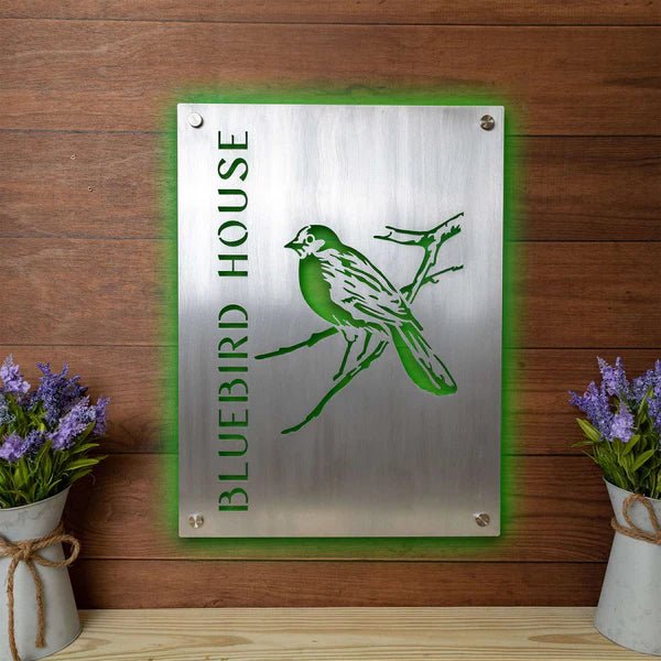 Metal sign with green bird illustration and text “Bluebird House” on wooden background, custom outdoor house plaque, decorative bird-themed home décor