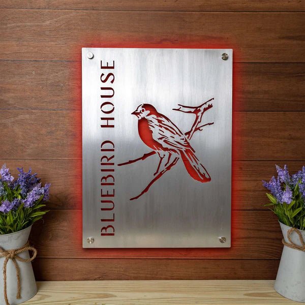Metal sign with red bird illustration and text “Bluebird House” on wooden background, custom outdoor house plaque, decorative bird-themed home décor
