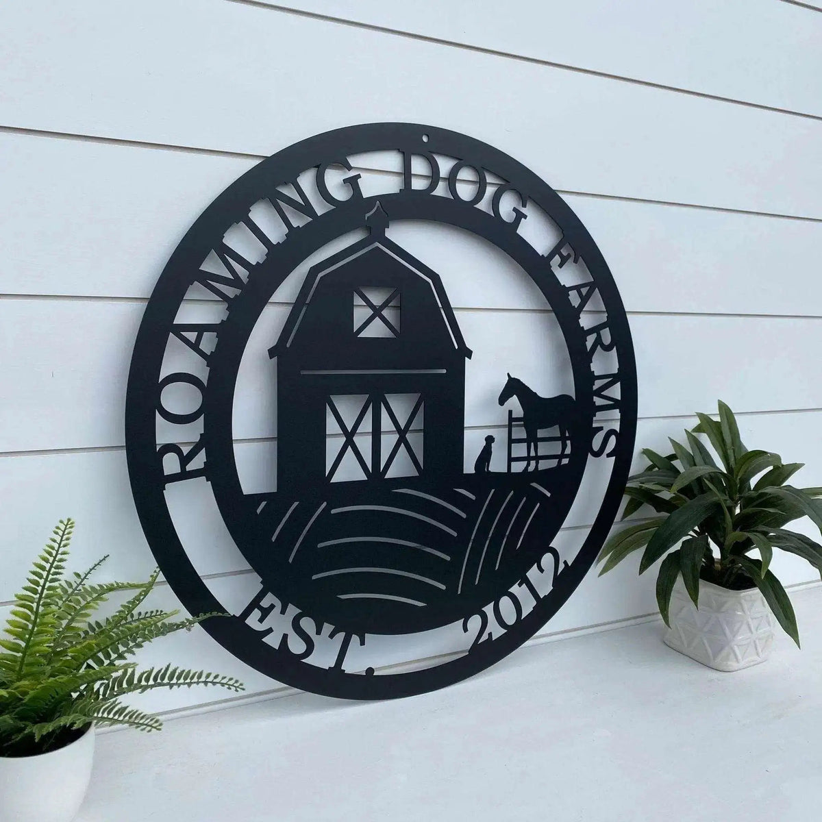 Custom barn dog horse ranch metal sign for farmhouse décor, angled view of personalized “Roaming Dog Farms” plaque on white wooden background.