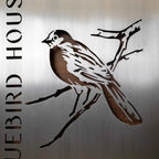 Metallic sign featuring a bird design on a metallic background, showcasing sleek, durable construction and decorative branding.