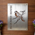 Metal sign featuring a bluebird illustration and the text “Bluebird House,” displayed on a wooden background, showcasing vibrant colors and rustic decorative design.