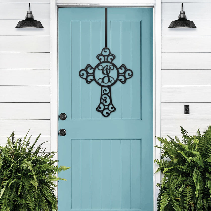 Black cross monogram metal door wreath displayed on a wood door