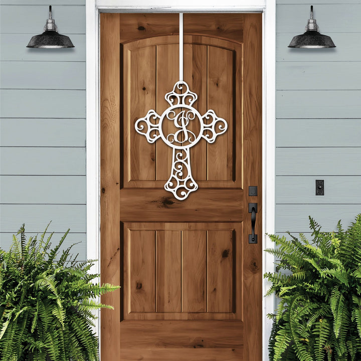 White cross monogram metal door wreath displayed on a wood door