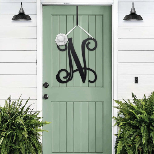 Black personalized metal initial door wreath displayed on a green front door