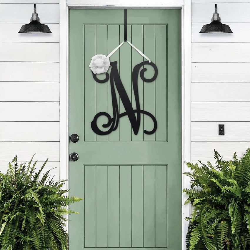 Black personalized metal initial door wreath displayed on a green front door