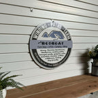 Round metal sign for “Winding Paths Farm and Retreat” displayed on a wooden surface with surrounding plants, highlighting rustic design and decorative outdoor appeal.