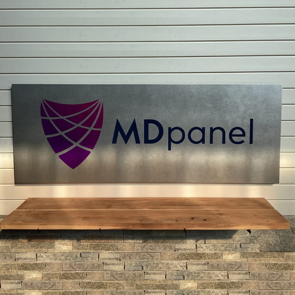 Metal sign featuring the MDpanel logo displayed on a wooden bench against a wooden panel background, showcasing durable craftsmanship and professional branding.