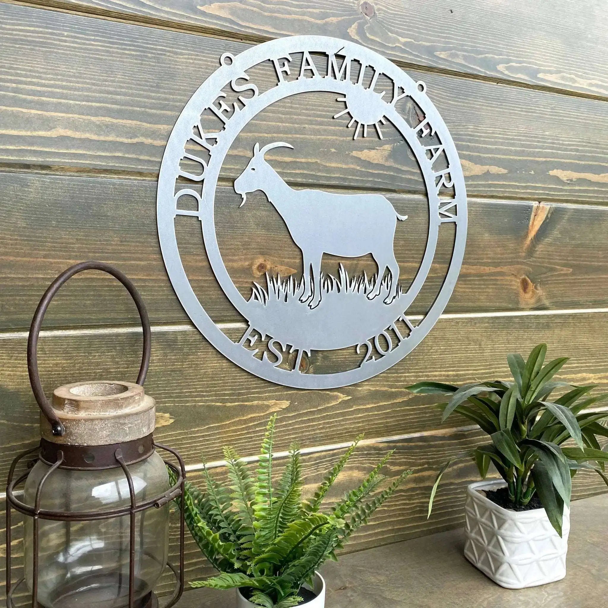 Custom goat metal sign for barns and farmhouses, outdoor décor with goat silhouette and 'Duke’s Family Farm' text on wooden wall with plants and lantern