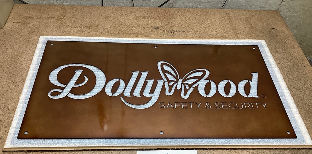 Custom laser-cut metal Dollywood Safety & Security sign, decorative outdoor plaque mounted on stone surface, powder coated for durability