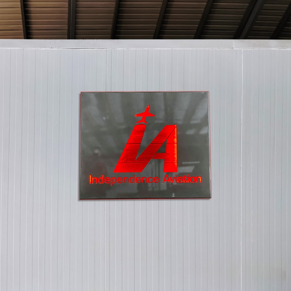 Red custom light box sign with “IA” logo and “Independence Aviation” text displayed on a gray wall