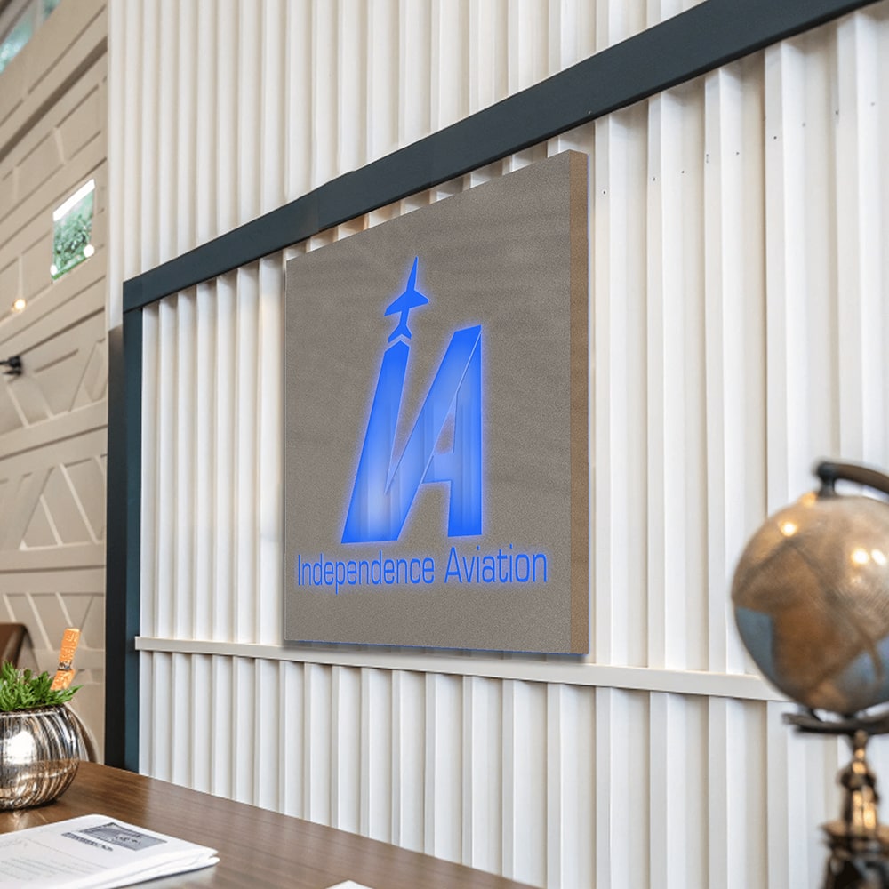 Custom light box sign displaying the Independence Aviation logo mounted on a wall in an office setting