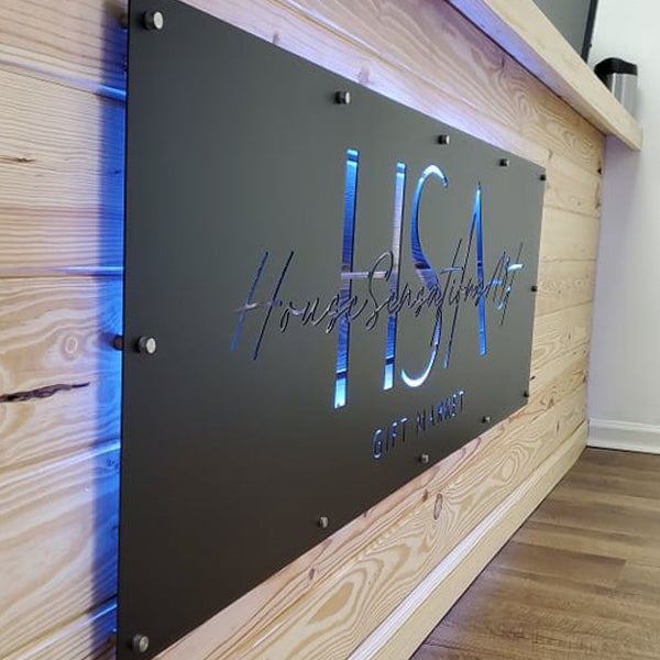Custom matte black LED backlit metal sign with HSA logo, modern powder coated steel wall sign mounted on wood backdrop, personalized business branding sign for front door or outdoor entry décor