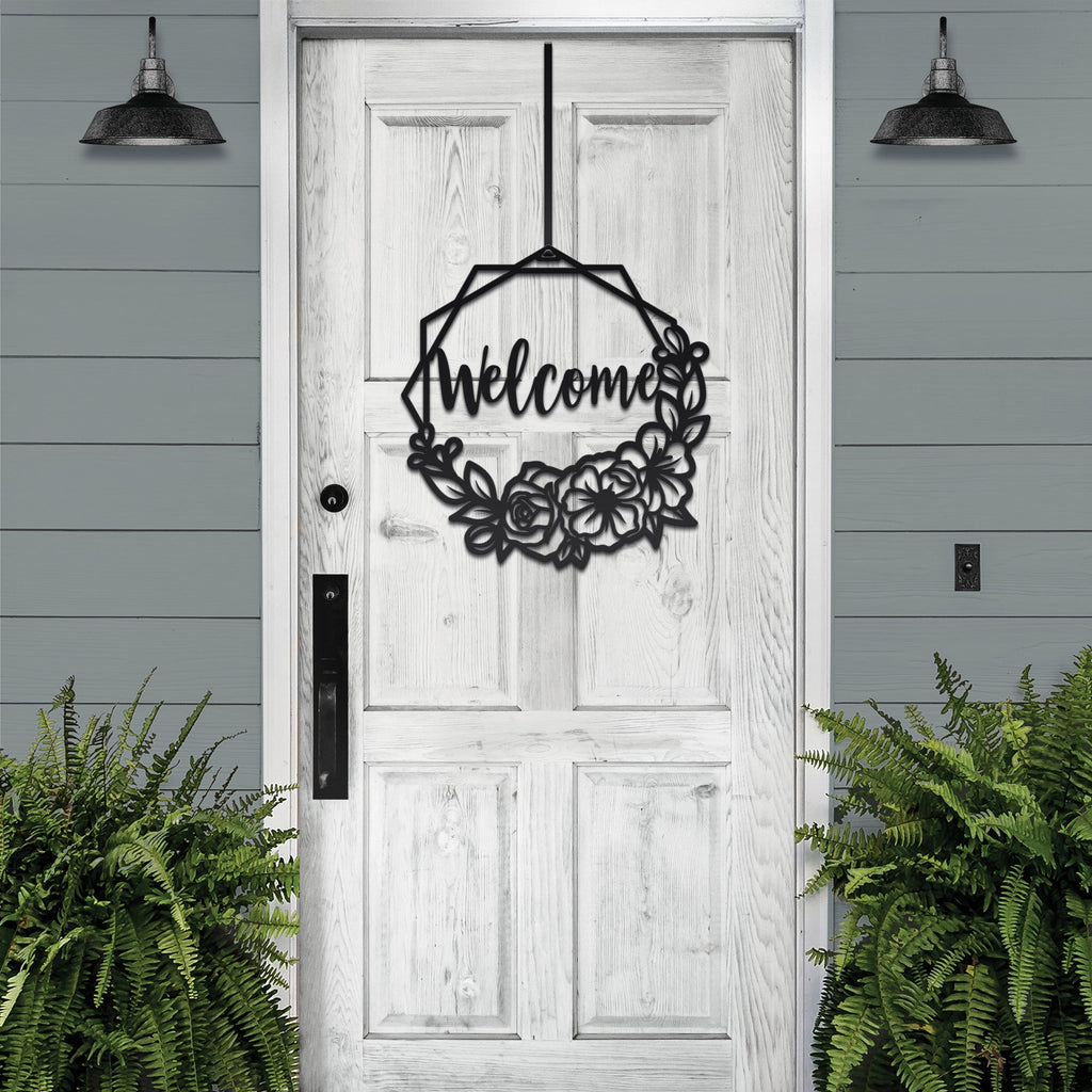 Decorative metal wreath with “Welcome” text hanging on white wooden door with surrounding greenery, custom outdoor home entrance décor