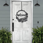 Decorative metal wreath with “Welcome” text hanging on white wooden door with surrounding greenery, custom outdoor home entrance décor