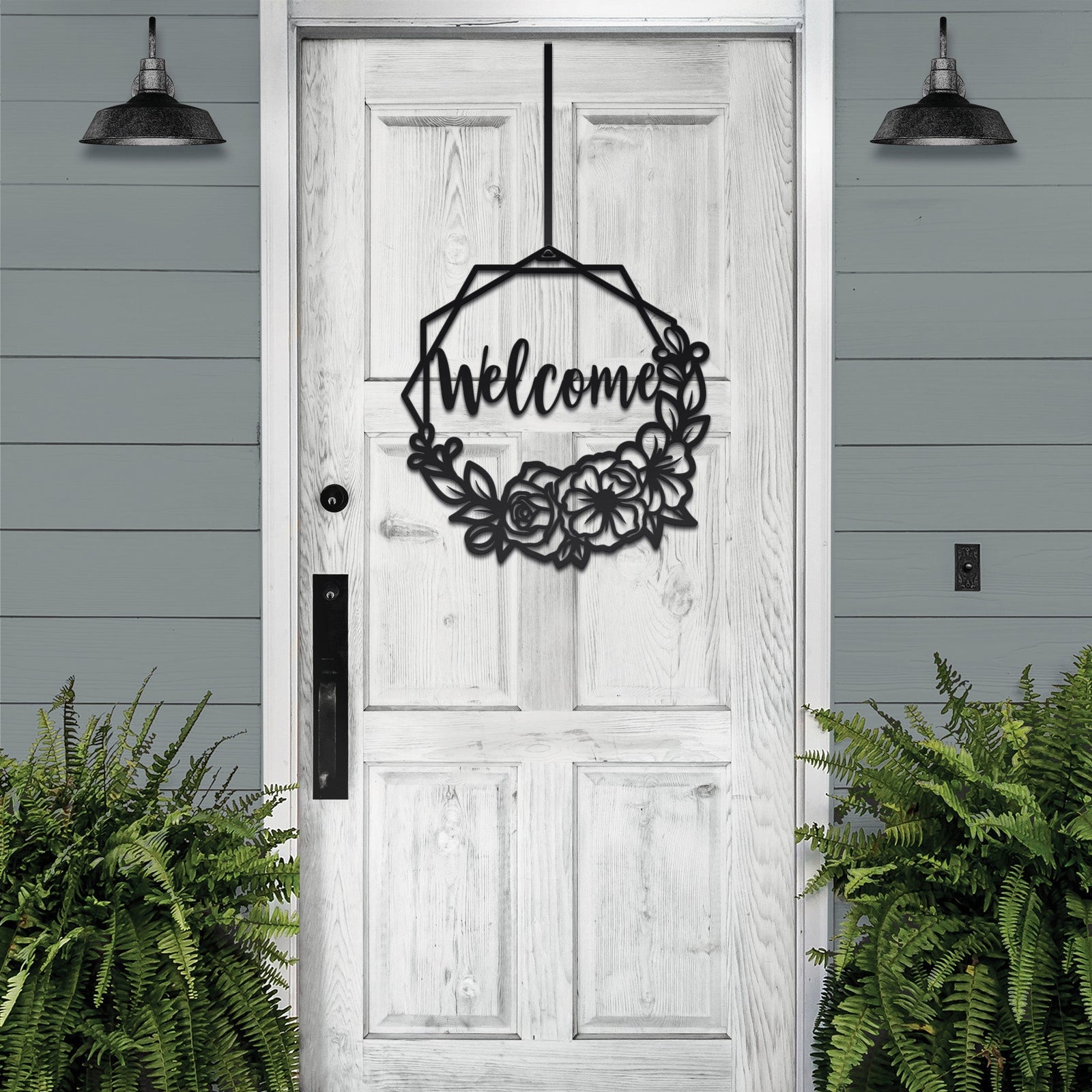 Decorative metal wreath with “Welcome” text hanging on white wooden door with surrounding greenery, custom outdoor home entrance décor