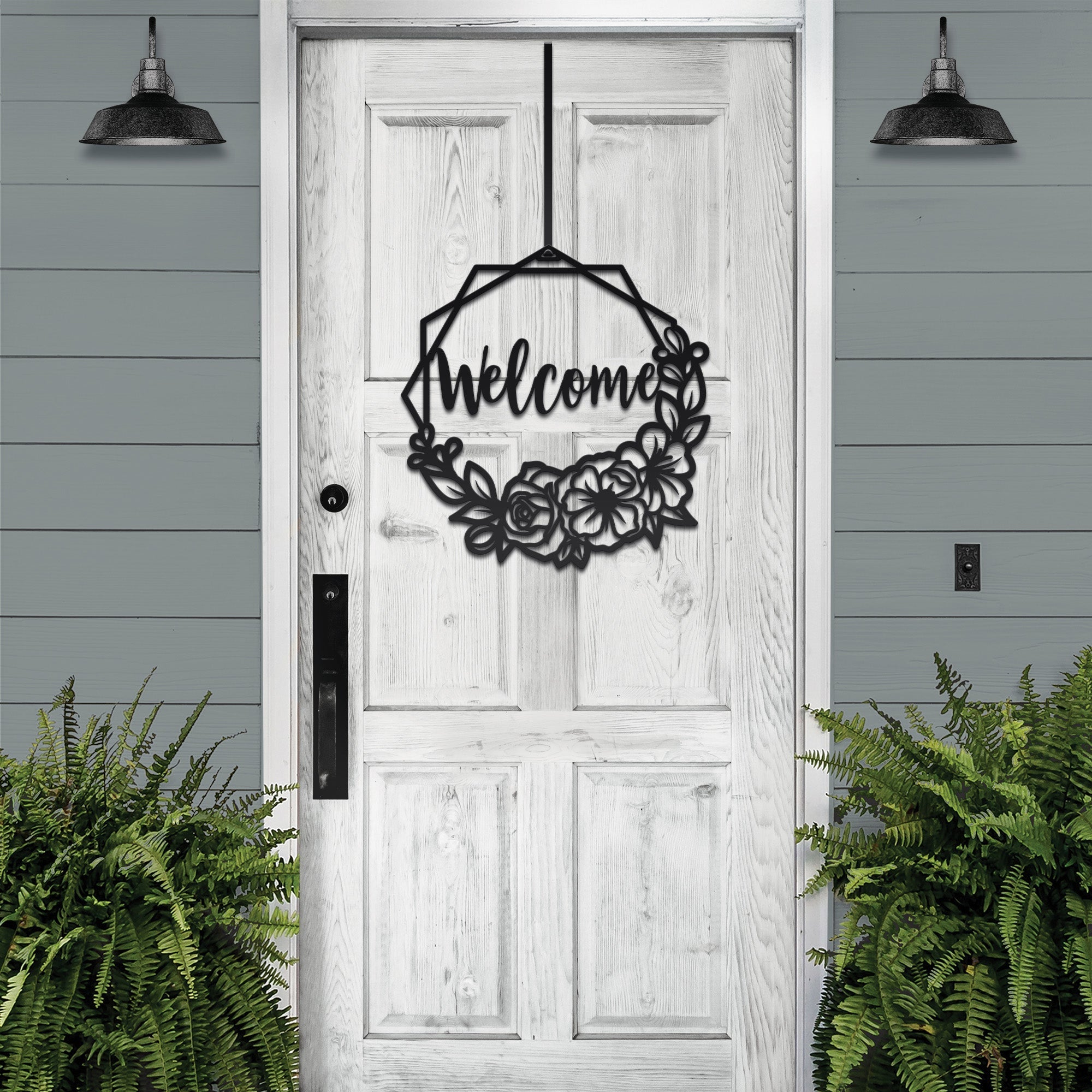 Decorative metal wreath with “Welcome” text hanging on white wooden door with surrounding greenery, custom outdoor home entrance décor
