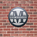 Custom metal gate sign with “Mirchandani” branding, circular personalized family or business décor mounted on brick wall exterior.