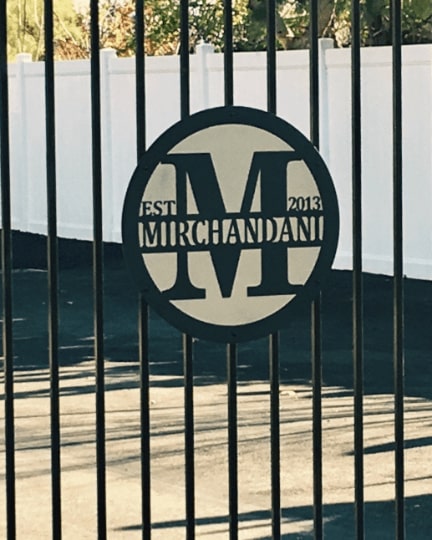 Custom metal gate sign with “Mirchandani” branding, personalized family or business décor mounted behind black metal gate exterior.