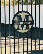 Custom metal gate sign with “Mirchandani” branding, personalized family or business décor mounted behind black metal gate exterior.