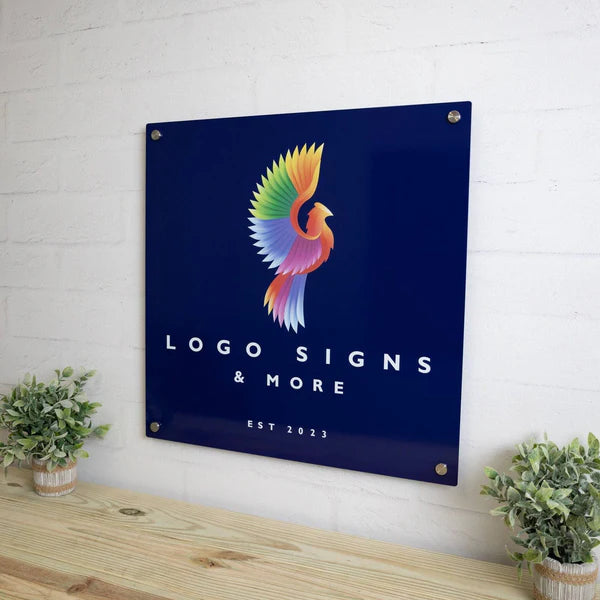 Square sign with colorful bird logo, 'LOGO SIGNS & MORE' and 'EST 2023,' mounted on wall with corner screws.