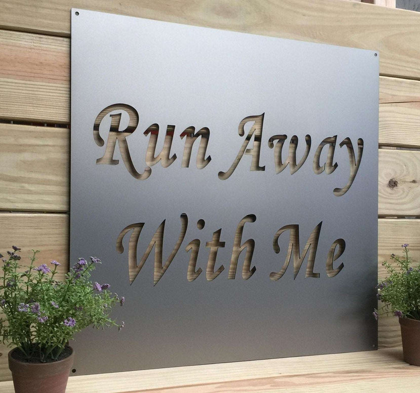 Metal sign featuring the text “Run Away With Me” displayed on a wooden background, highlighting rustic charm and durable decorative craftsmanship.