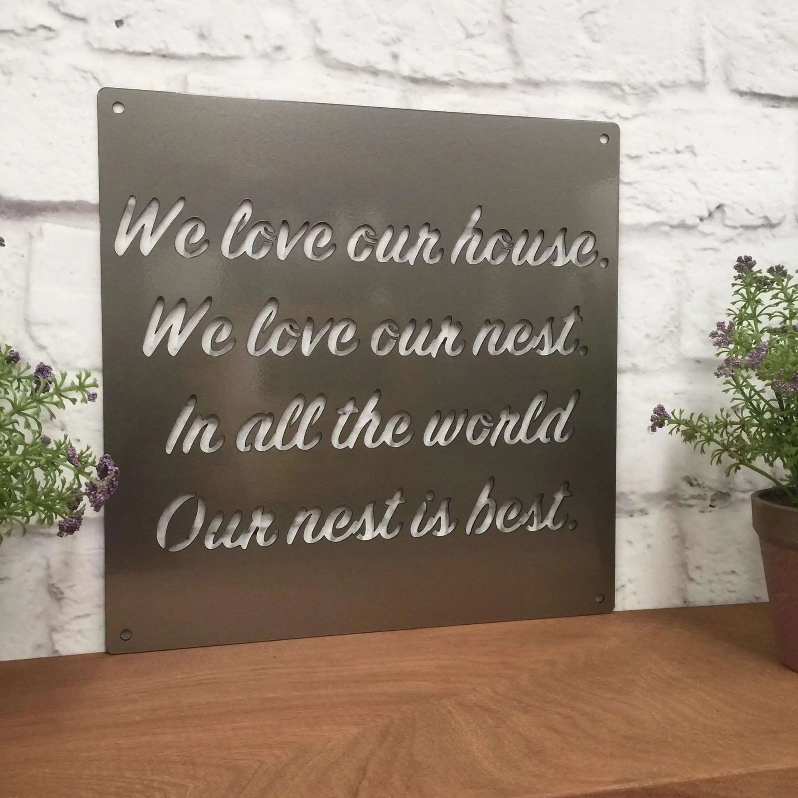 Decorative metal sign featuring engraved text, displayed on a wooden surface with plants, highlighting rustic style and elegant craftsmanship.