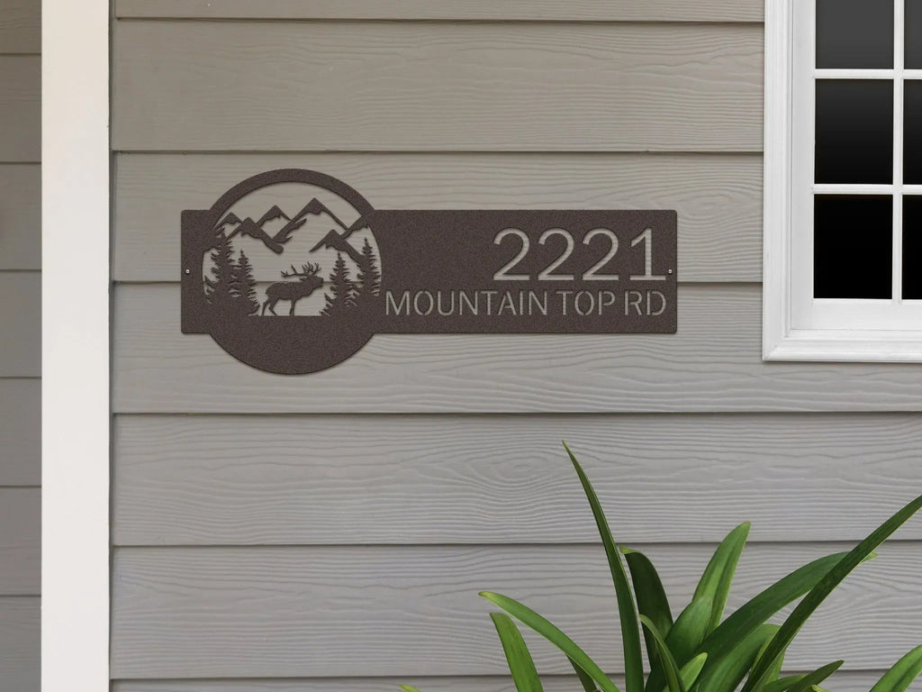 House number sign with mountain and landscape design on gray siding wall, rustic outdoor moose cabin decor