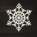 White snowflake-shaped decorative item placed on a dark wooden background, highlighting intricate detailing and festive seasonal design.