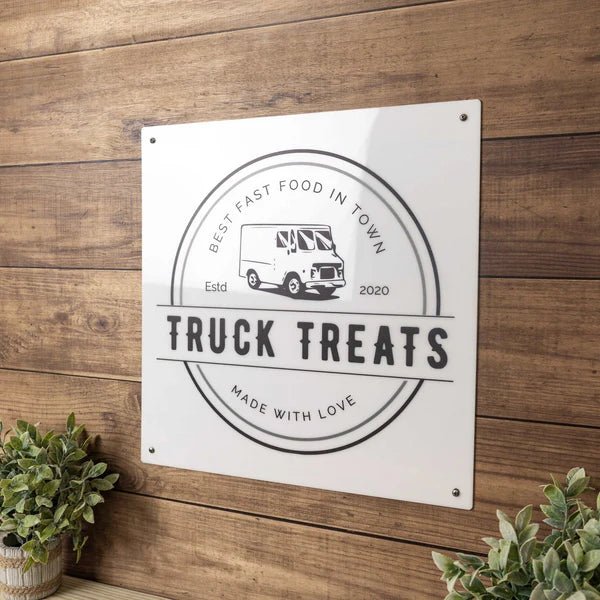 Metal sign featuring the “Truck Treats” design displayed on a wooden background, showcasing bold lettering with a rustic and eye-catching aesthetic.