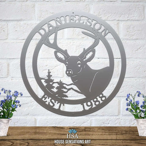Silver circular metal sign on light brick wall with deer head, pine tree, “EST 1988” and “DANIELSON” cut into the border.
