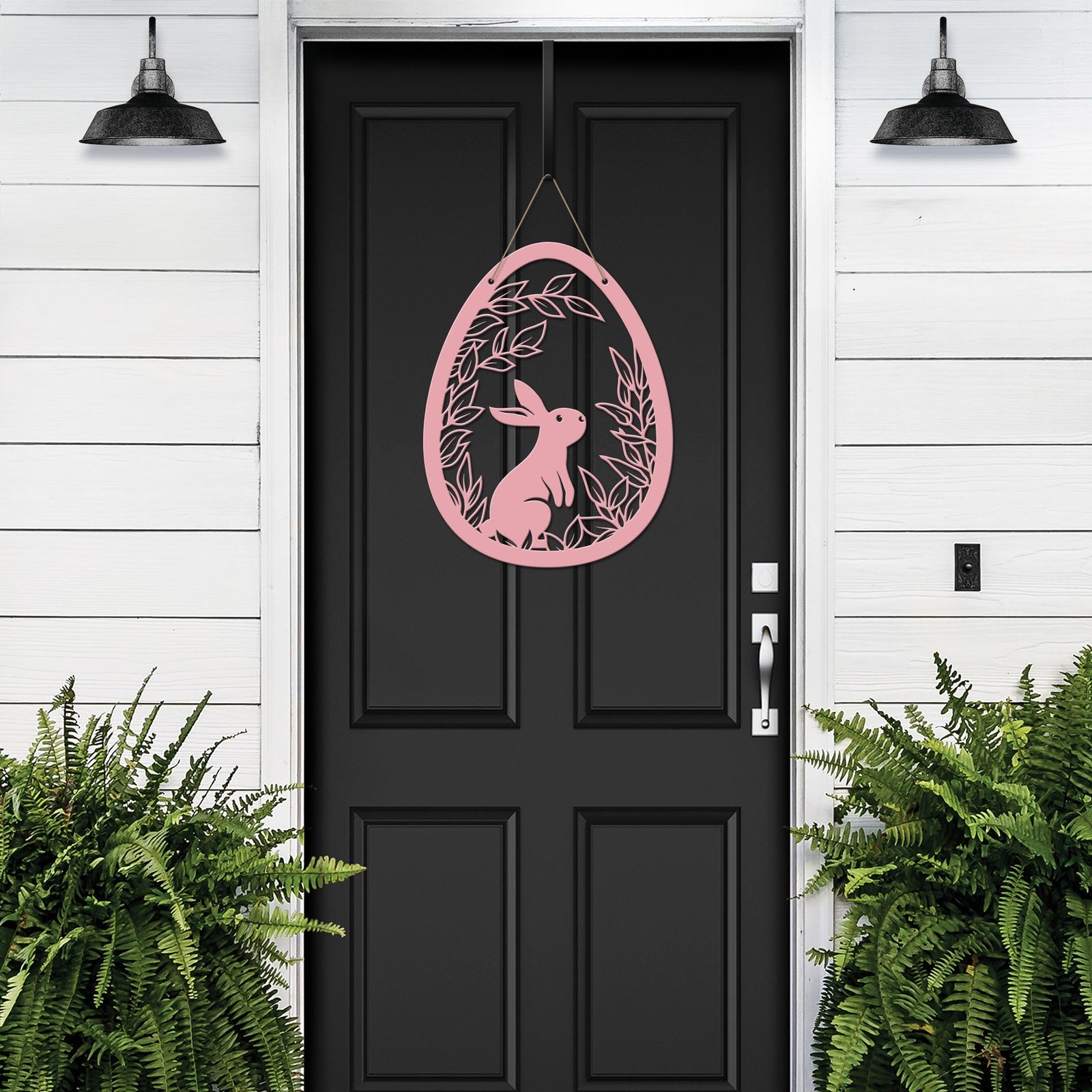 Pink metal Easter egg door hanger with rabbit design on black door, custom outdoor powder coated spring décor, farmhouse front door sign with green plants on white wall