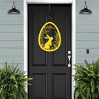 Black door with yellow metal Easter egg door hanger featuring rabbit and leaf cutouts, custom outdoor powder coated spring décor, farmhouse front door sign on light blue wall