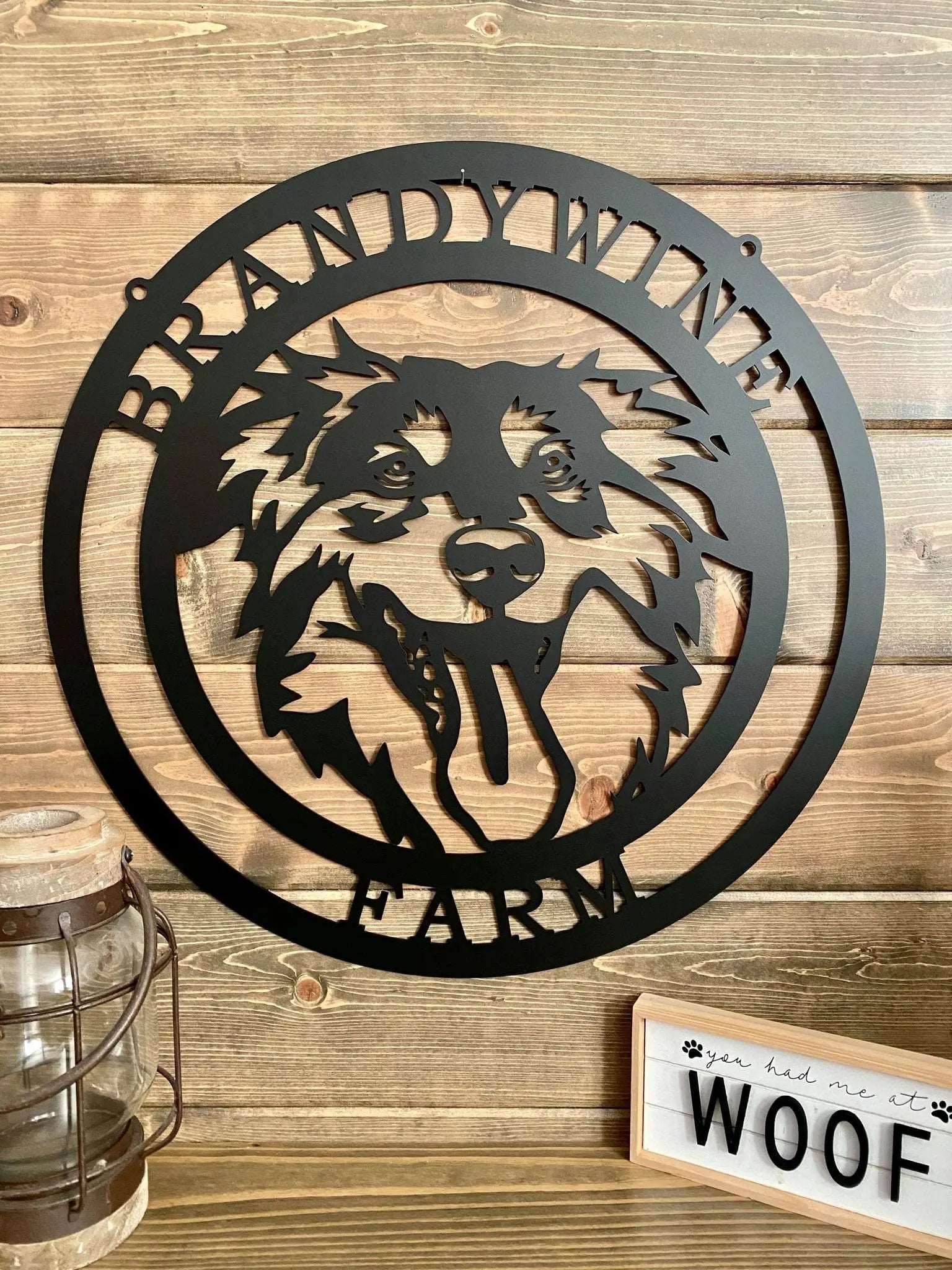 Close-up of black ranch sign with dog head silhouette and “BRANDYWINE FARM” text; mounted on paneled wall.