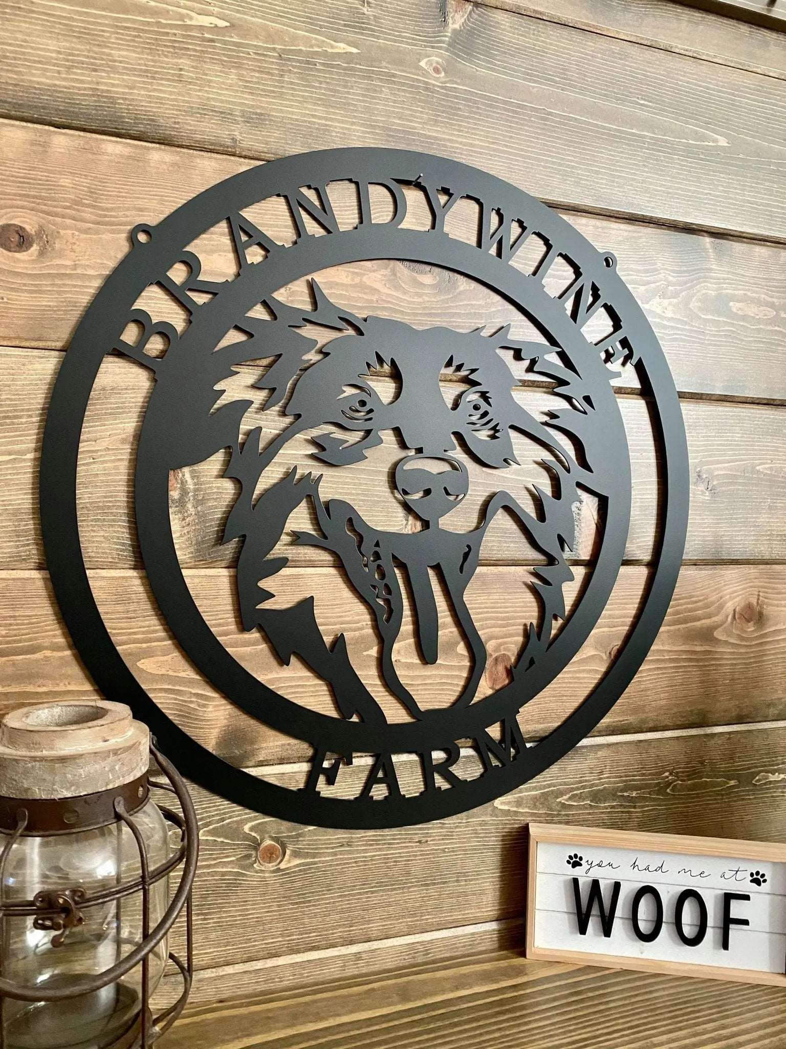 Side view of black metal ranch sign with dog head silhouette and “BRANDYWINE FARM” text; mounted on paneled wall.